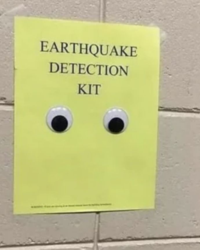 Yellow poster labeled "Earthquake Detection Kit" with two adhesive googly eyes attached
