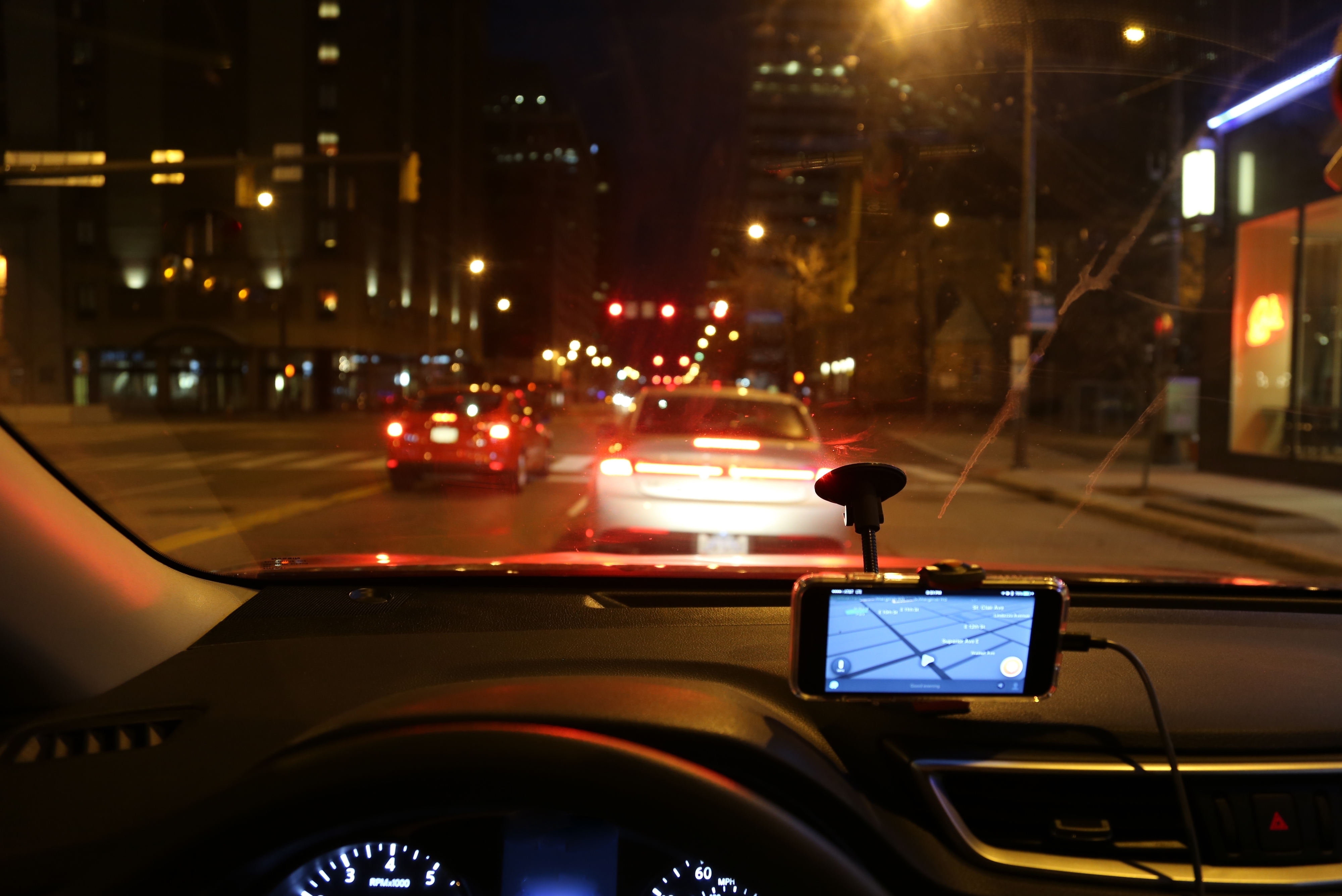 Nighttime city street view from a car dashboard, showing traffic ahead and a GPS device displaying navigation