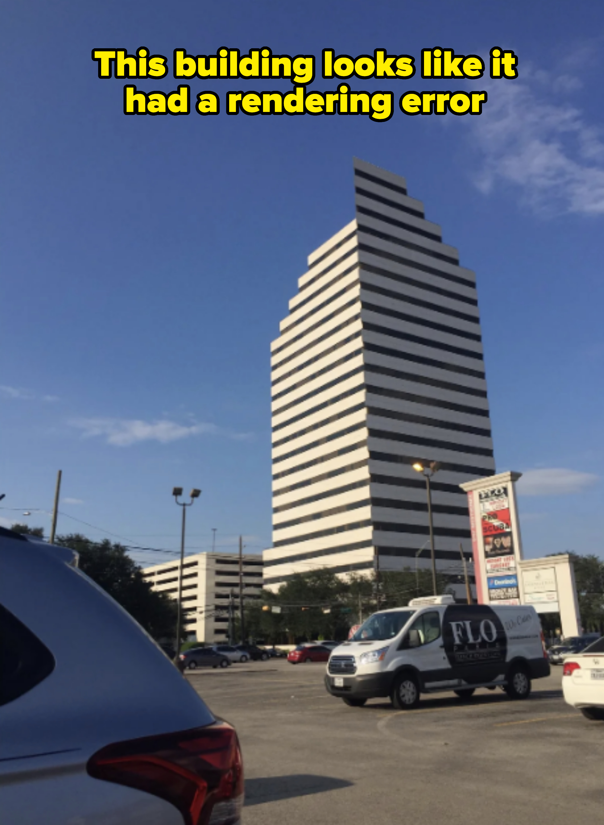 A tall, striped office building is viewed from a parking lot. Cars and a van with "FLO" branding are parked in the foreground