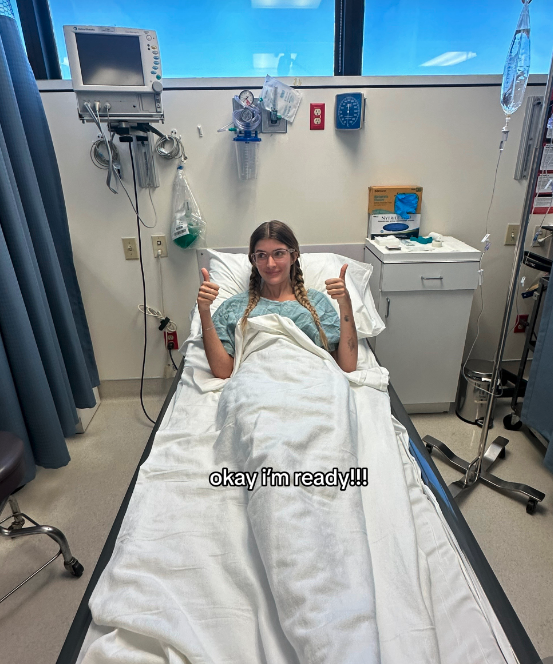 Sami lies in a hospital bed with thumbs up, text overlay reads: &quot;okay I'm ready!!!&quot; Medical equipment is visible in the background