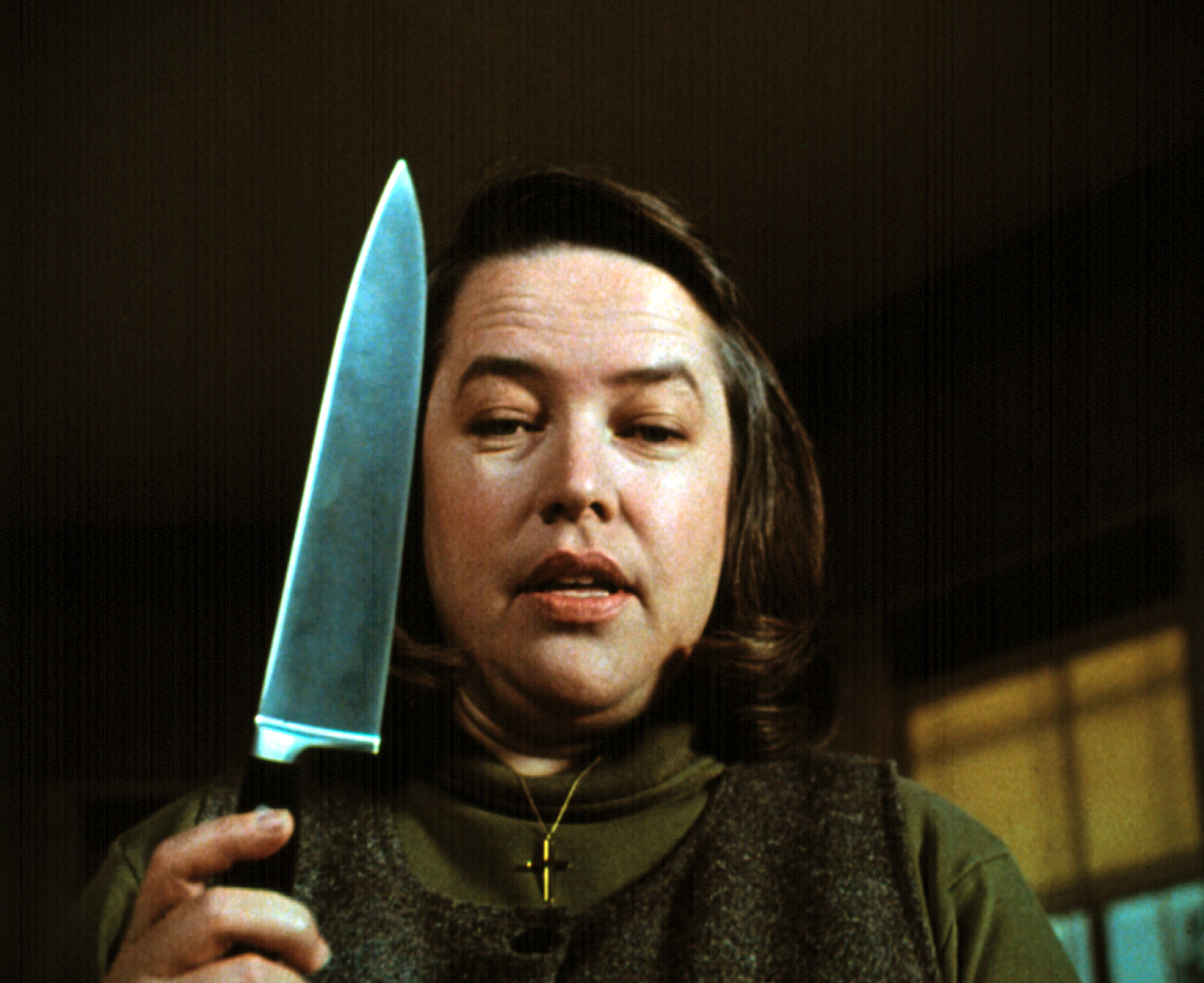 Kathy Bates holds a large knife while wearing a cross necklace in a scene from the movie "Misery."