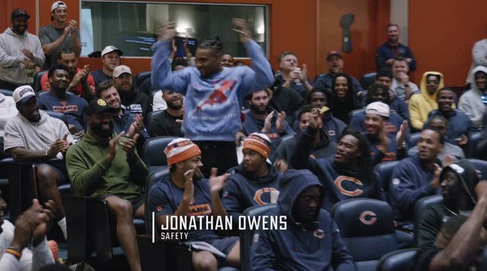 Jonathan Owens stands and celebrates in front of a crowd of smiling, clapping teammates in a lively room. Text on image: "Jonathan Owens, Safety"