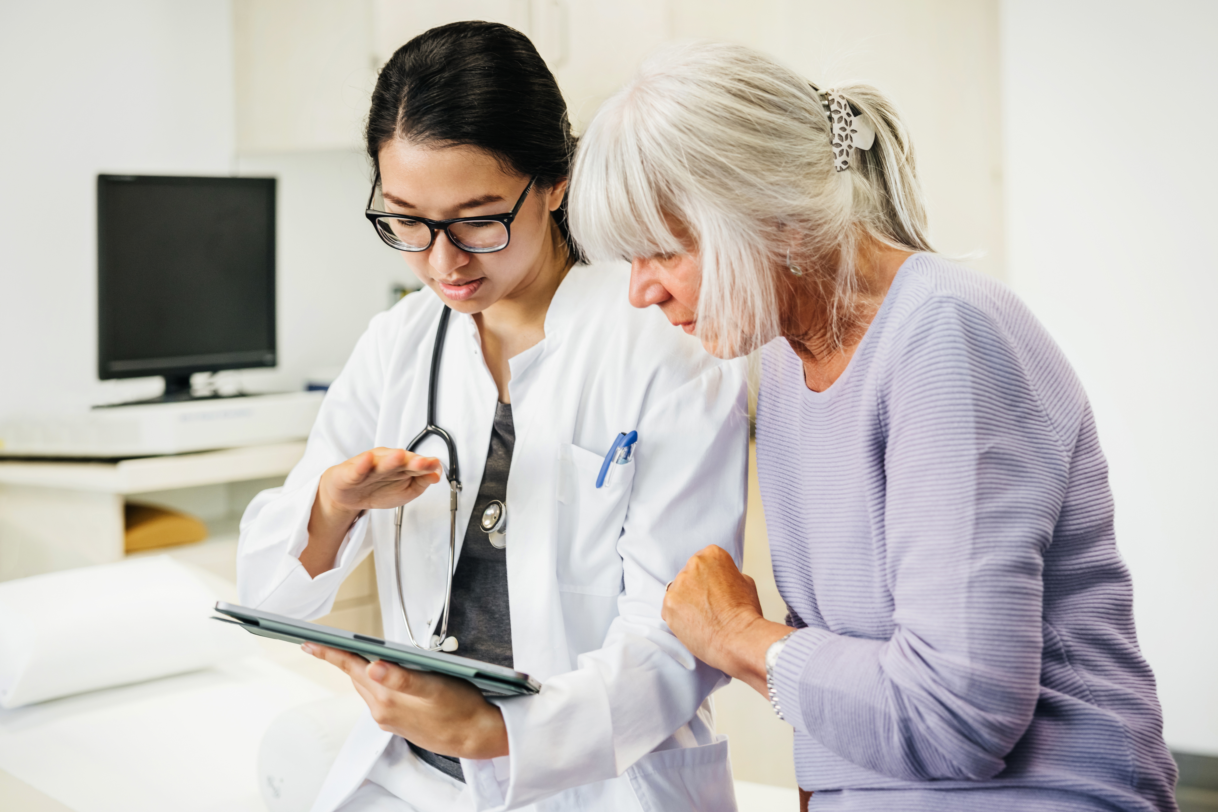 A doctor and an elderly woman look at a tablet together, discussing medical information in an office setting