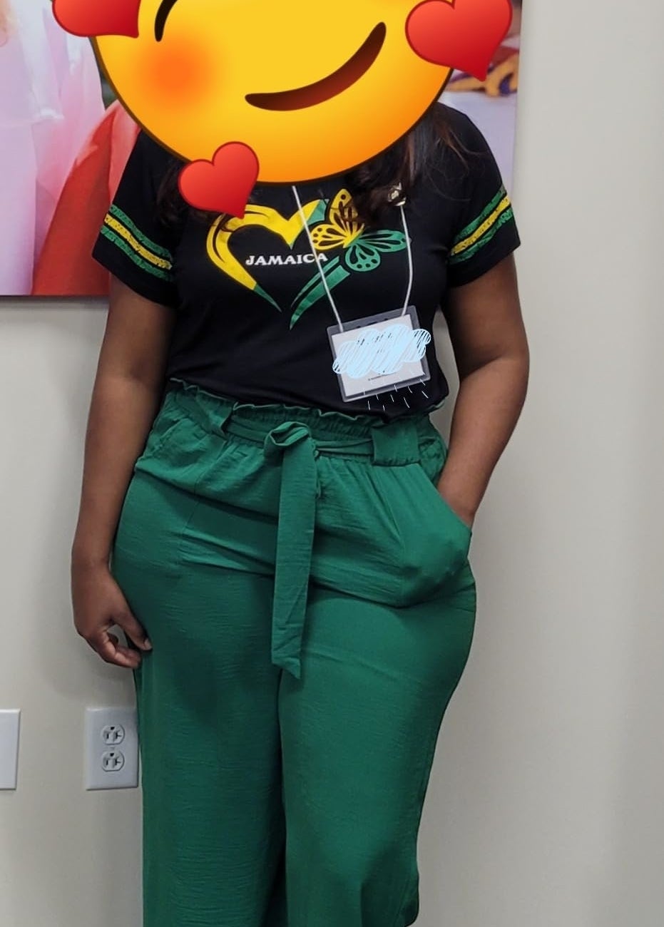 Reviewer wearing a black shirt with a logo and green wide-leg pants, standing indoors. Face obscured by a smiling emoji with heart eyes