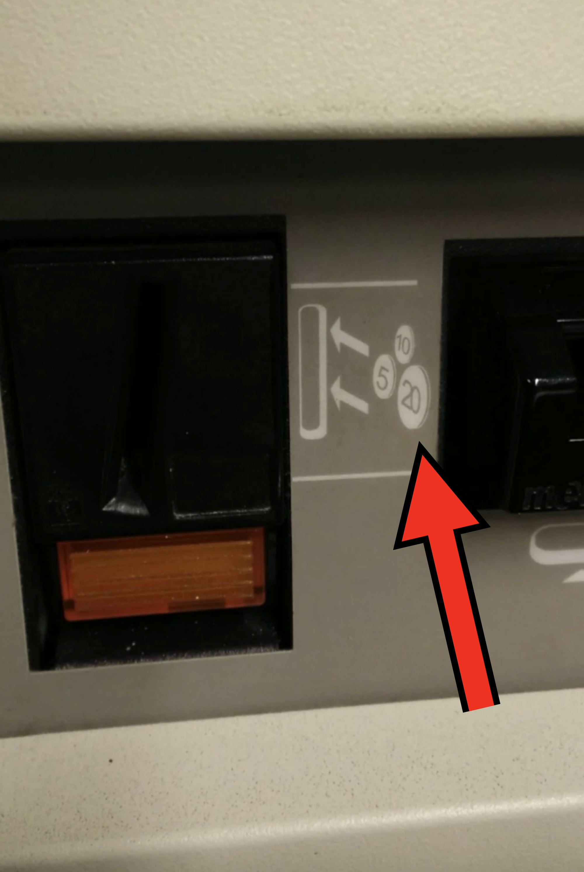 Close-up of a section of a vending machine showing a coin slot area and denomination markings for 5, 10, and 20 currency units