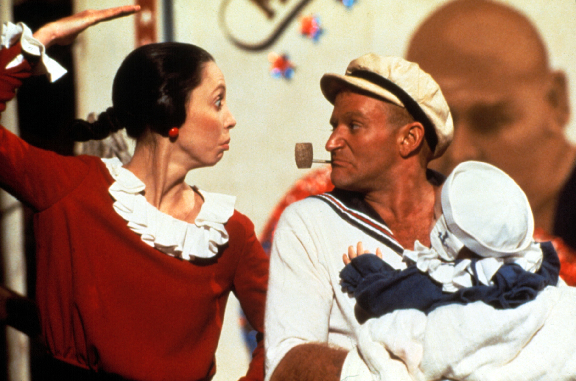 Shelley Duvall as Olive Oyl and Robin Williams as Popeye in sailor attire, holding an infant from the movie "Popeye"