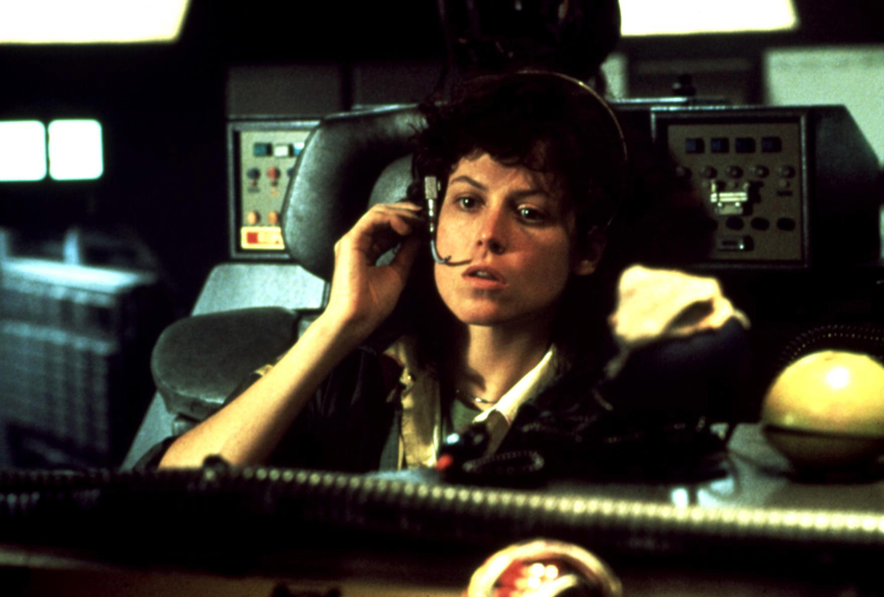 Sigourney Weaver in a sci-fi control room wearing a headset, likely from a scene in a movie