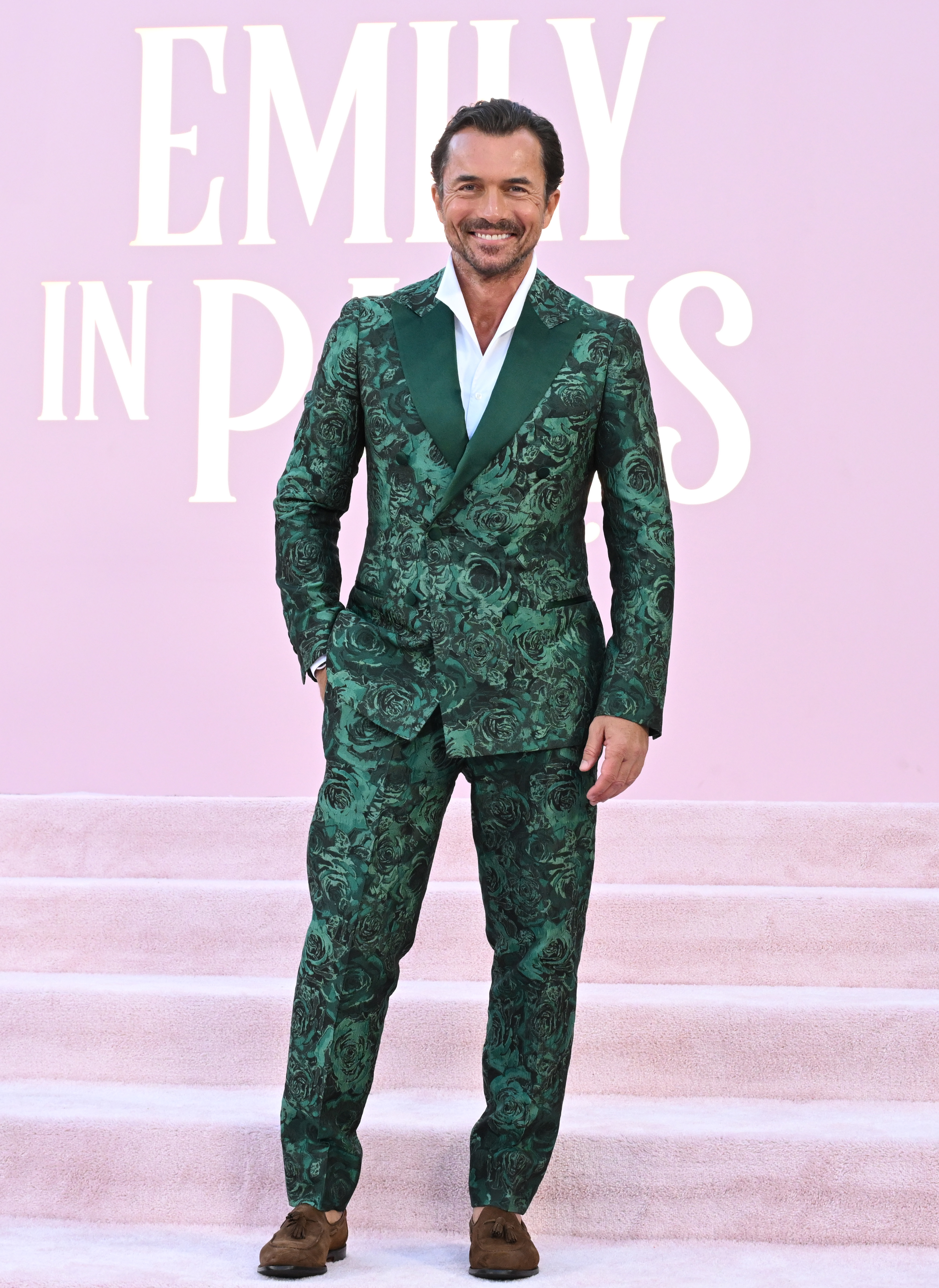 William Abadie wearing a green patterned suit and brown shoes at the "Emily in Paris" event