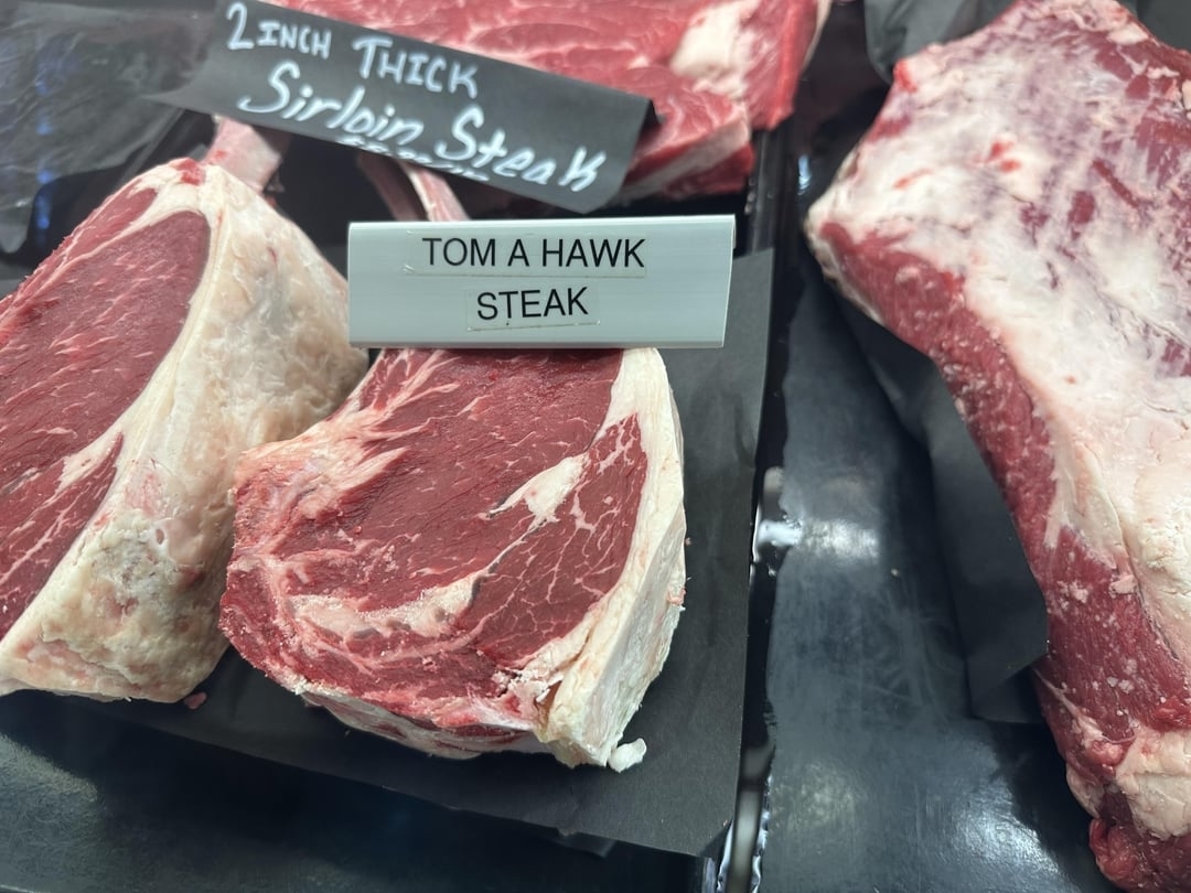 Close-up of raw steaks labeled "Tom A Hawk Steak" next to each other in a display case
