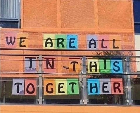 Sign on a building reads, "WE ARE ALL IN THIS TOGETHER," but there are posts in between "to" "get" and "her"