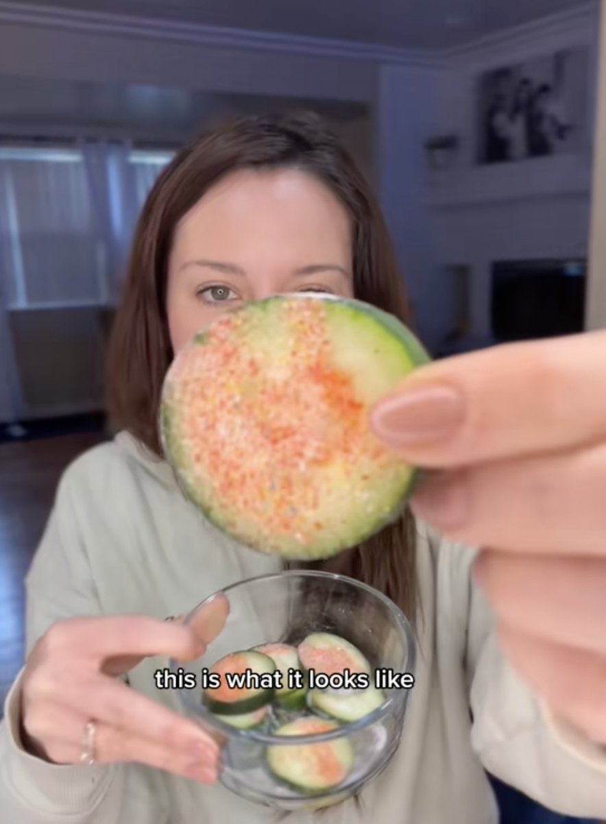 Close-up of a woman holding a piece of cucumber with seasoning. Text reads: "this is what it looks like."