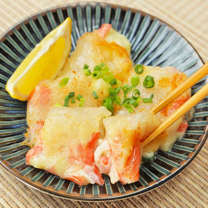 レモンのくさびとネギがのったカニ料理のクローズアップ。箸で一口サイズに割られています。