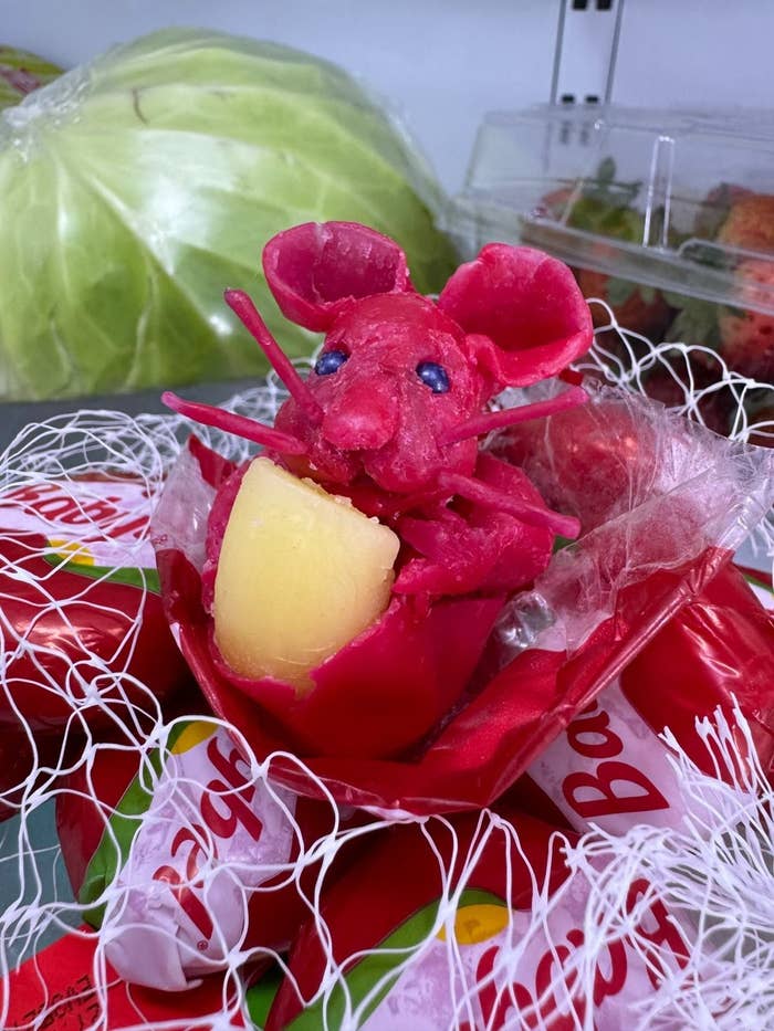 A Babybel cheese sculpture shaped like a mouse holding a piece of cheese, surrounded by Babybel cheese wrappers