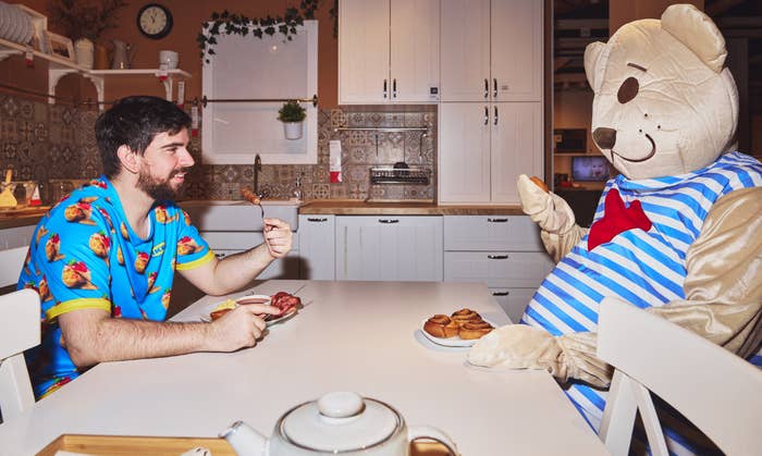 Man in fruit-themed pajamas has dinner with person in bear costume at a kitchen table