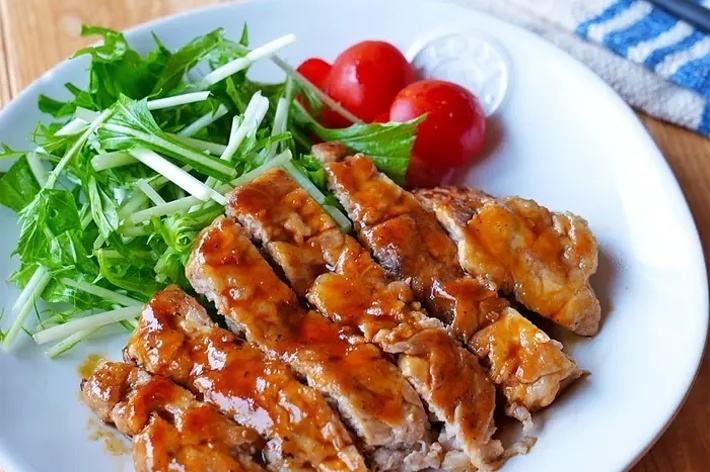 グリルチキンの薄切りとサラダが白い皿に盛り付けられている。後方にフォークとナイフが置かれている。