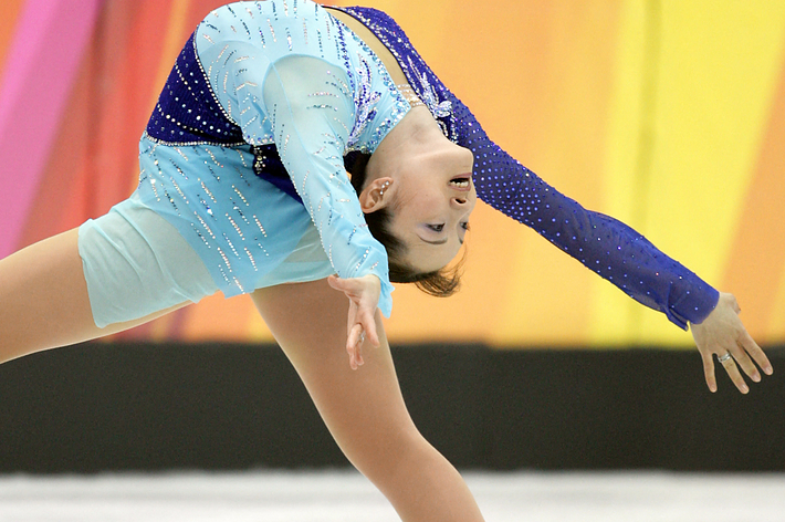 フィギュアスケート演技中の選手。水色と青のコスチュームを着用している。