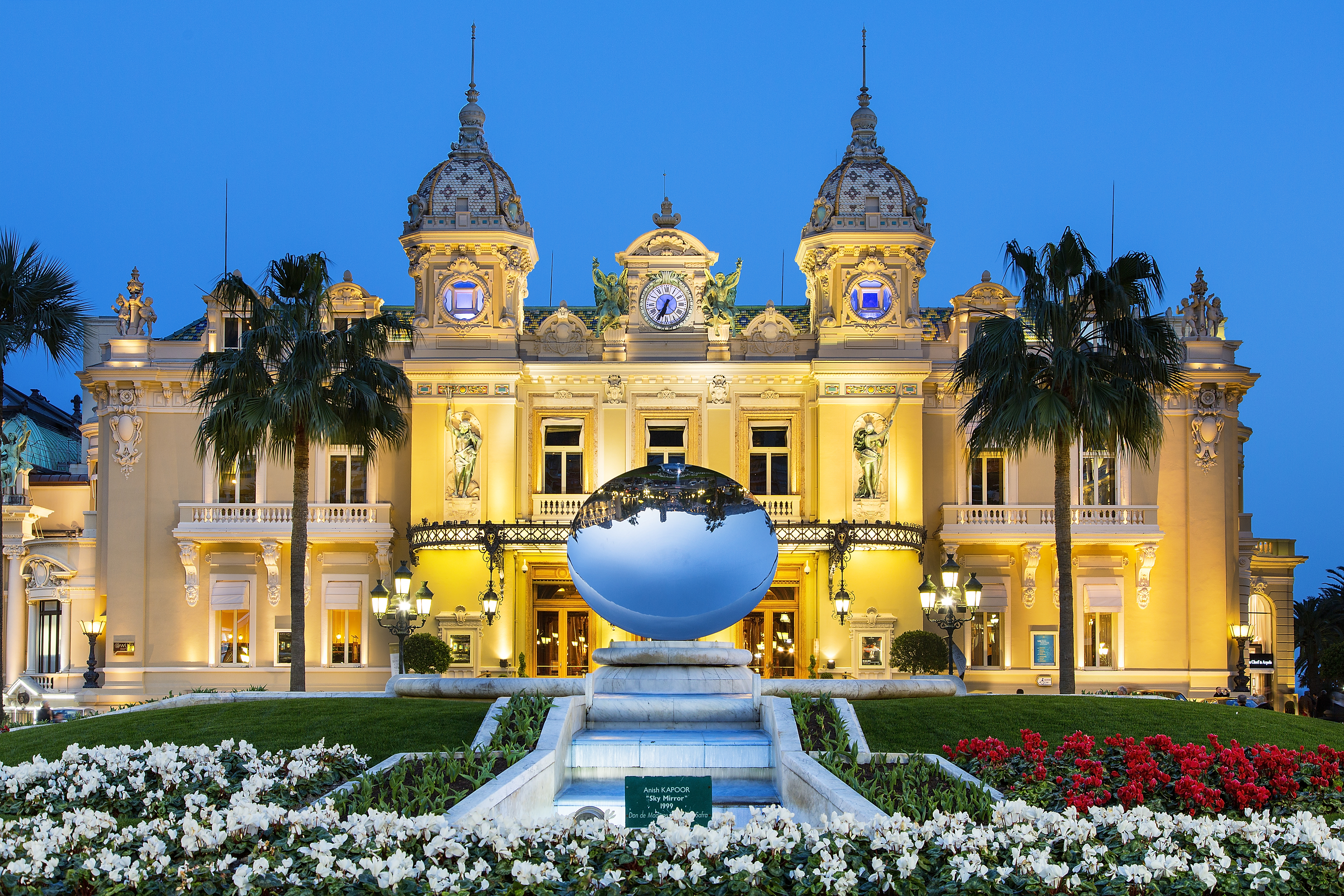 Monte Carlo Casino in Monaco, with its ornate architecture lit up at night, featuring a large reflective sculpture in front