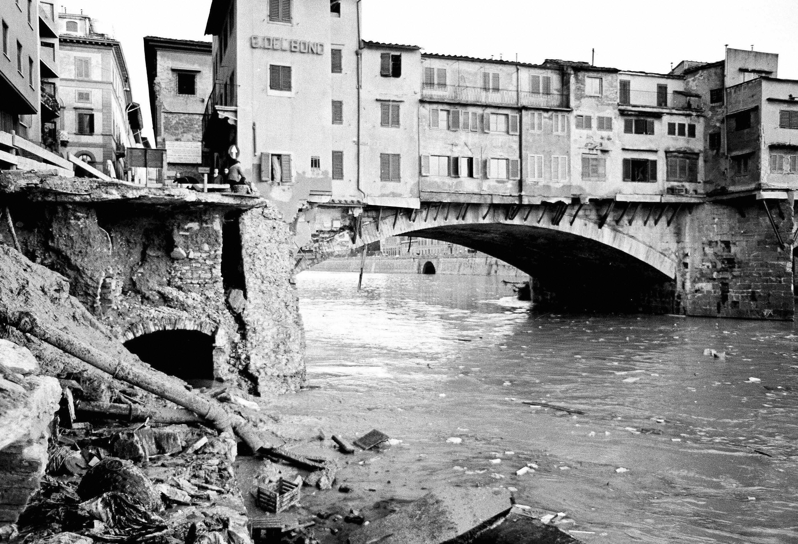 Historic photo of Ponte Vecchio bridge in Florence, Italy during a flood, with debris and water damage visible along the riverbank