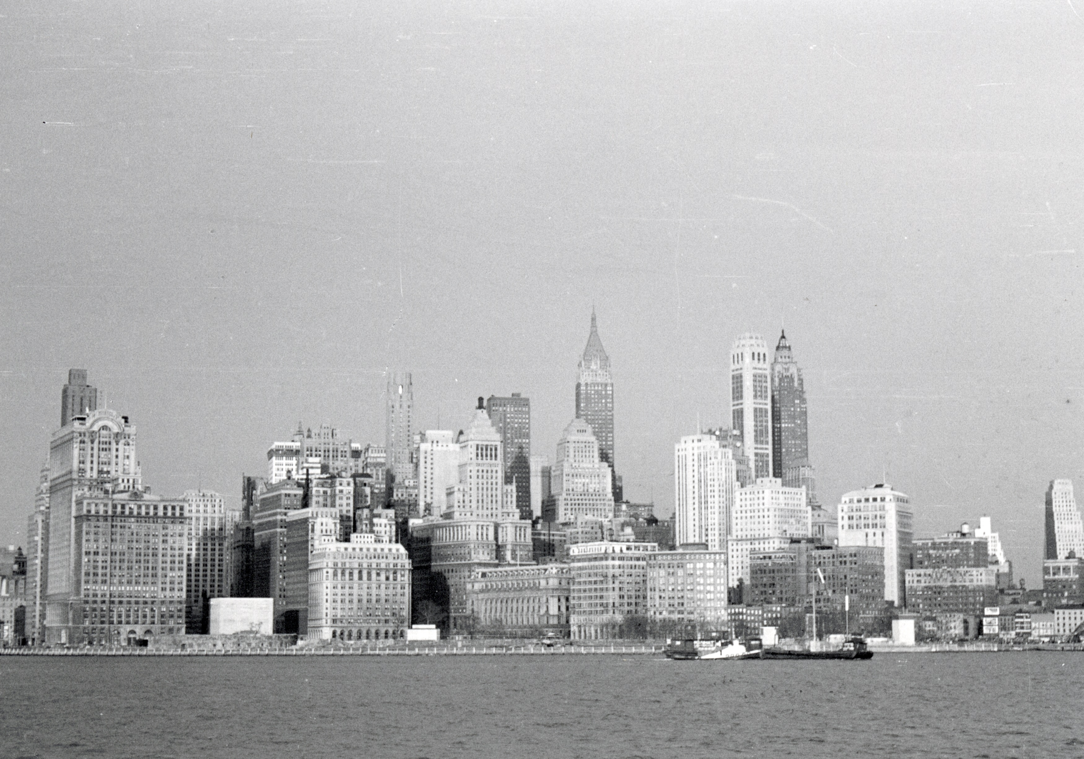 A vintage black-and-white photograph of the New York City skyline featuring numerous high-rise buildings and a few boats on the waterfront
