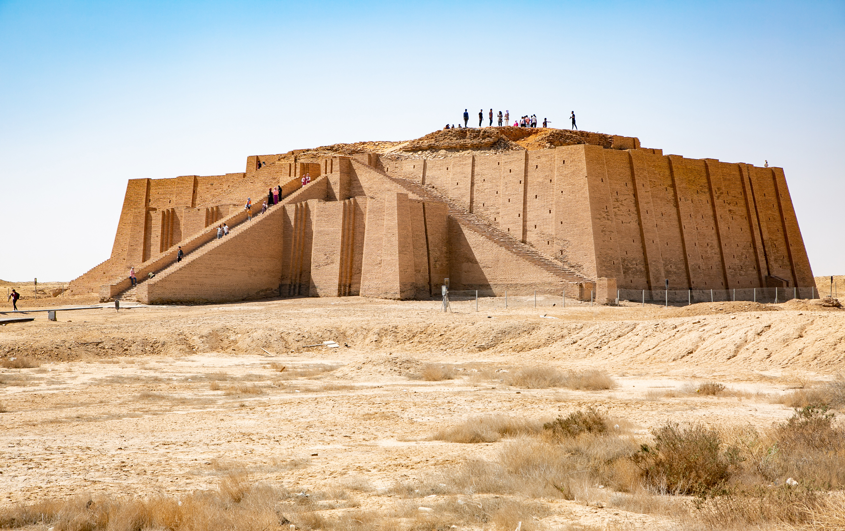 The image shows the Ziggurat of Ur, an ancient stepped pyramid structure in Iraq, with several people walking and standing on its various levels