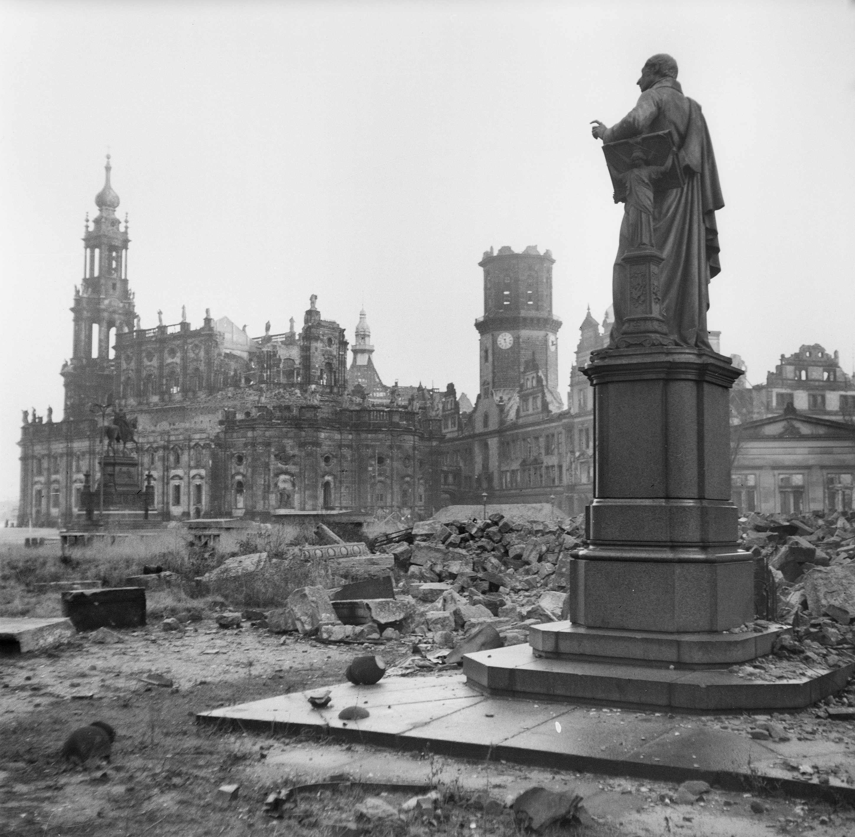 Statue amid ruins and rubble, with a damaged historical building in the background, in the aftermath of a wartime event