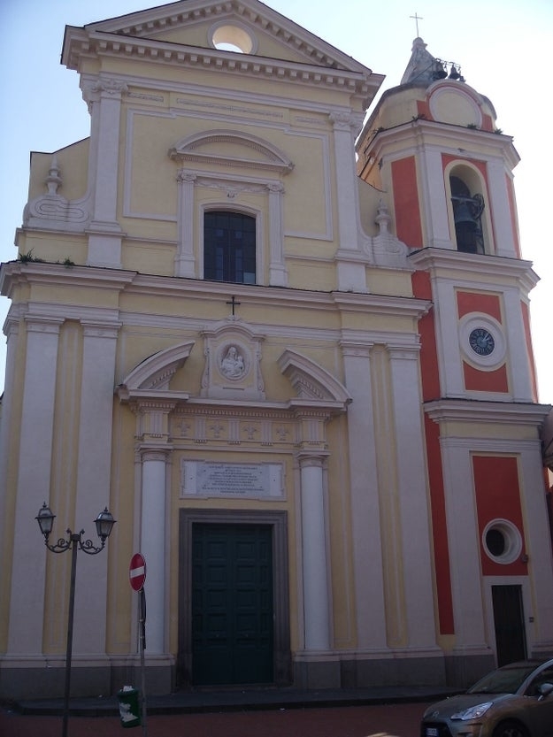 Facade of a large church with an ornate entrance, next to a bell tower featuring a clock and arched openings