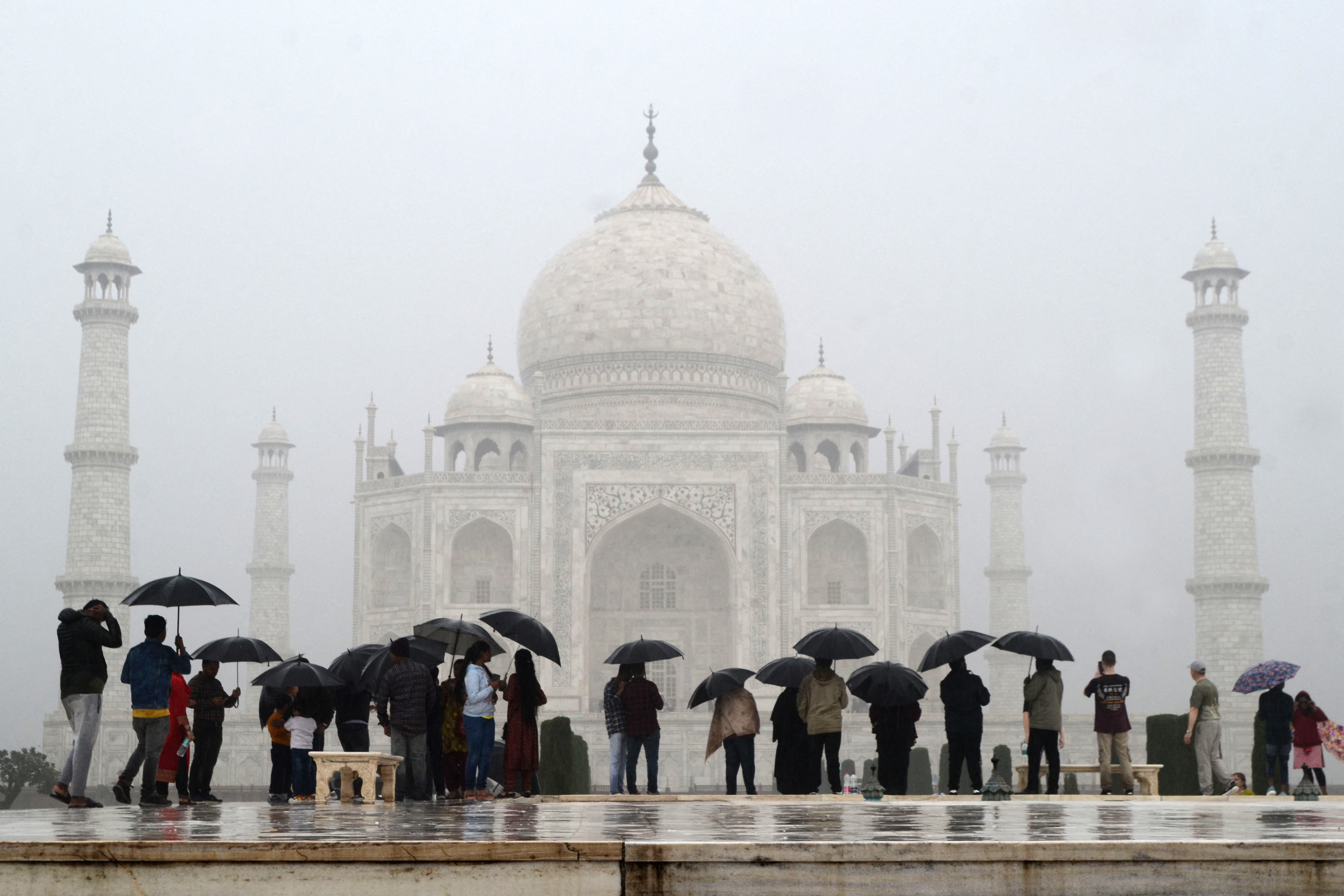 People holding umbrellas in front of the Taj Mahal on a rainy day