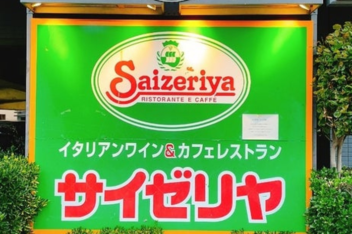 Sign for Saizeriya Ristorante e Caffe in Japanese and English. Operating hours: 11:00 AM to 2:00 AM daily. The sign is surrounded by decorative bushes