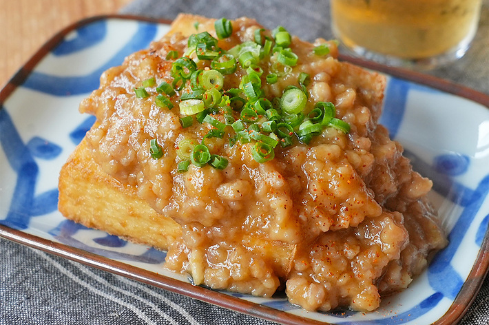 皿に豆腐料理が盛られており、刻みねぎと肉あんが上にかかっている。後ろには飲み物がある。