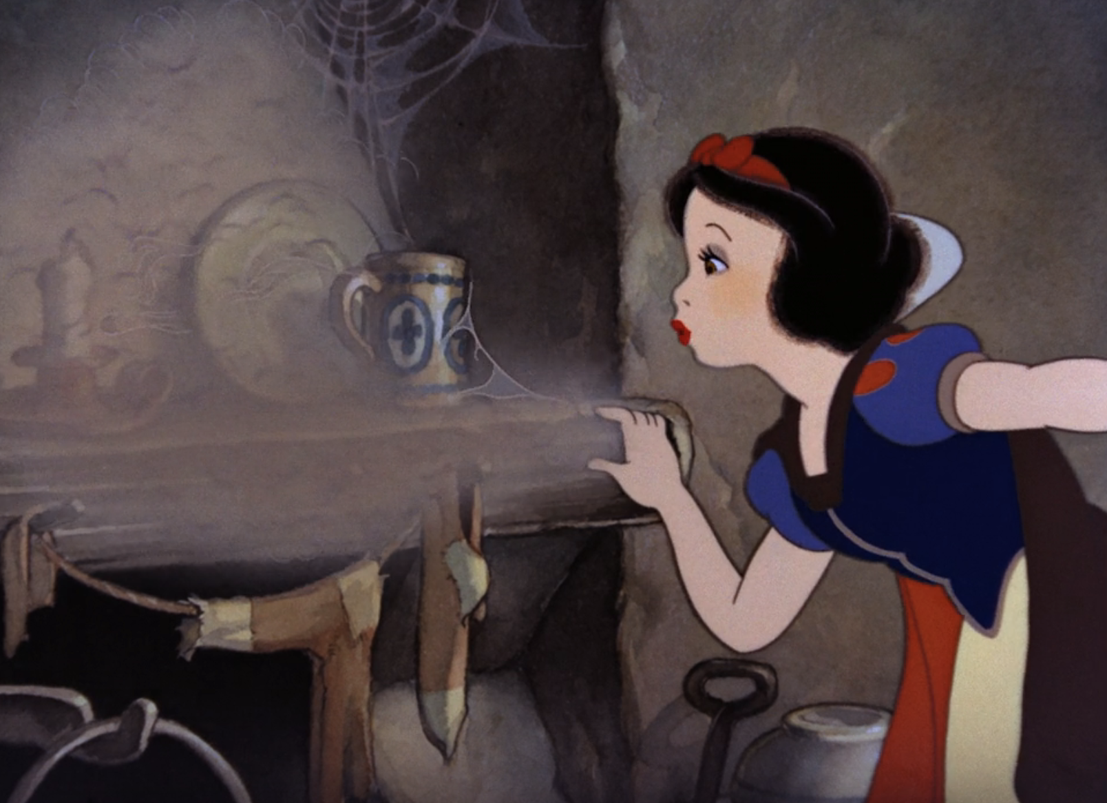 Snow White blows dust off objects in a dimly lit room with cobwebs, pointing toward a blue and white mug. She wears a classic dress with a red headband