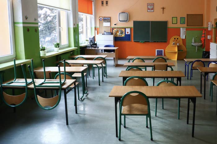 Empty classroom with chairs stacked on tables, a chalkboard, plants on the windowsill, and various arts and crafts on the walls
