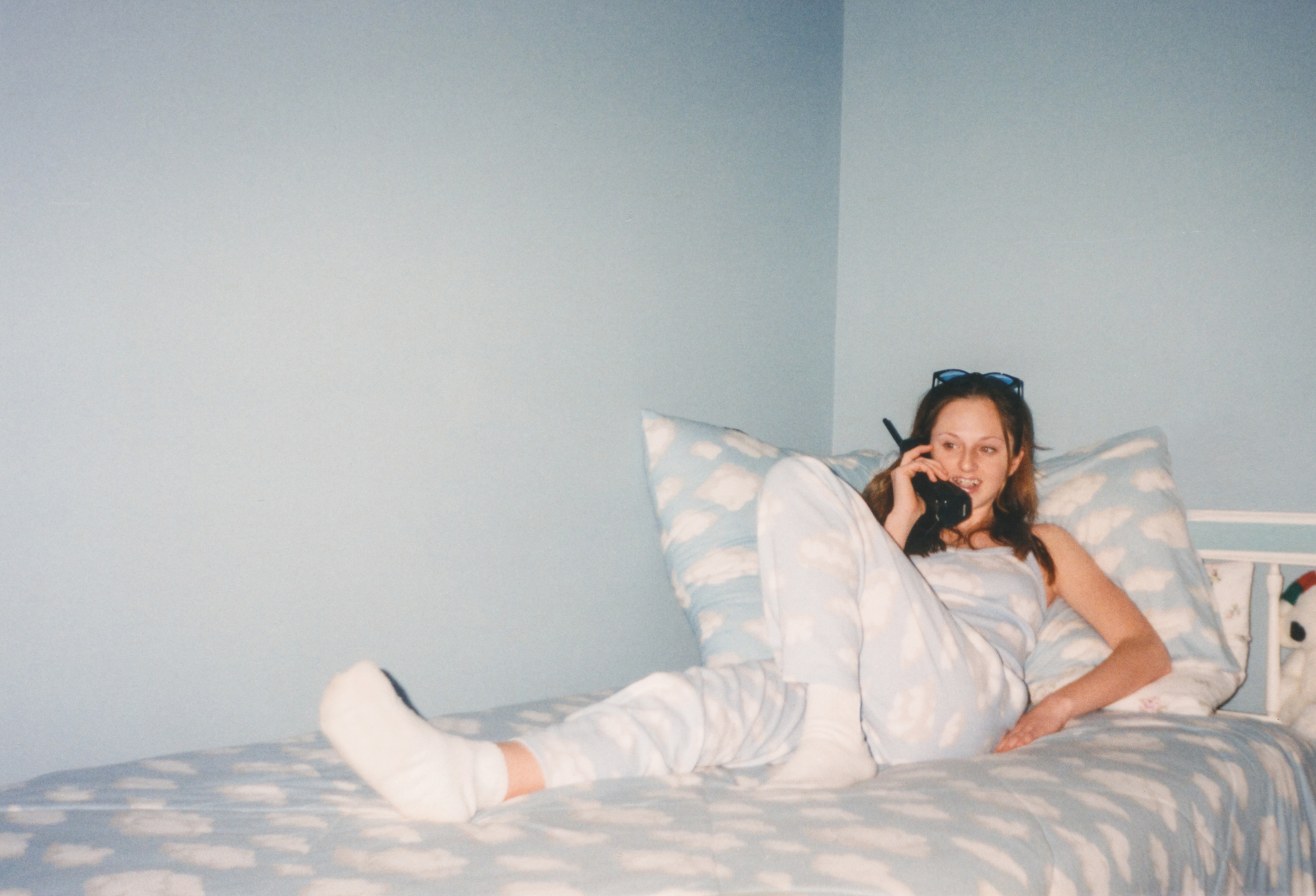 A person lounges on a bed with cloud-patterned bedding, talking on a cordless phone