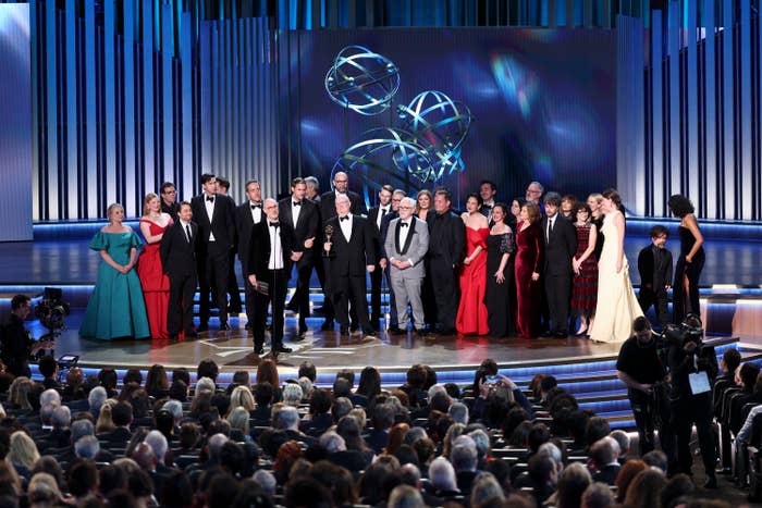 Group of well-dressed individuals on stage at an award ceremony, with a large audience watching