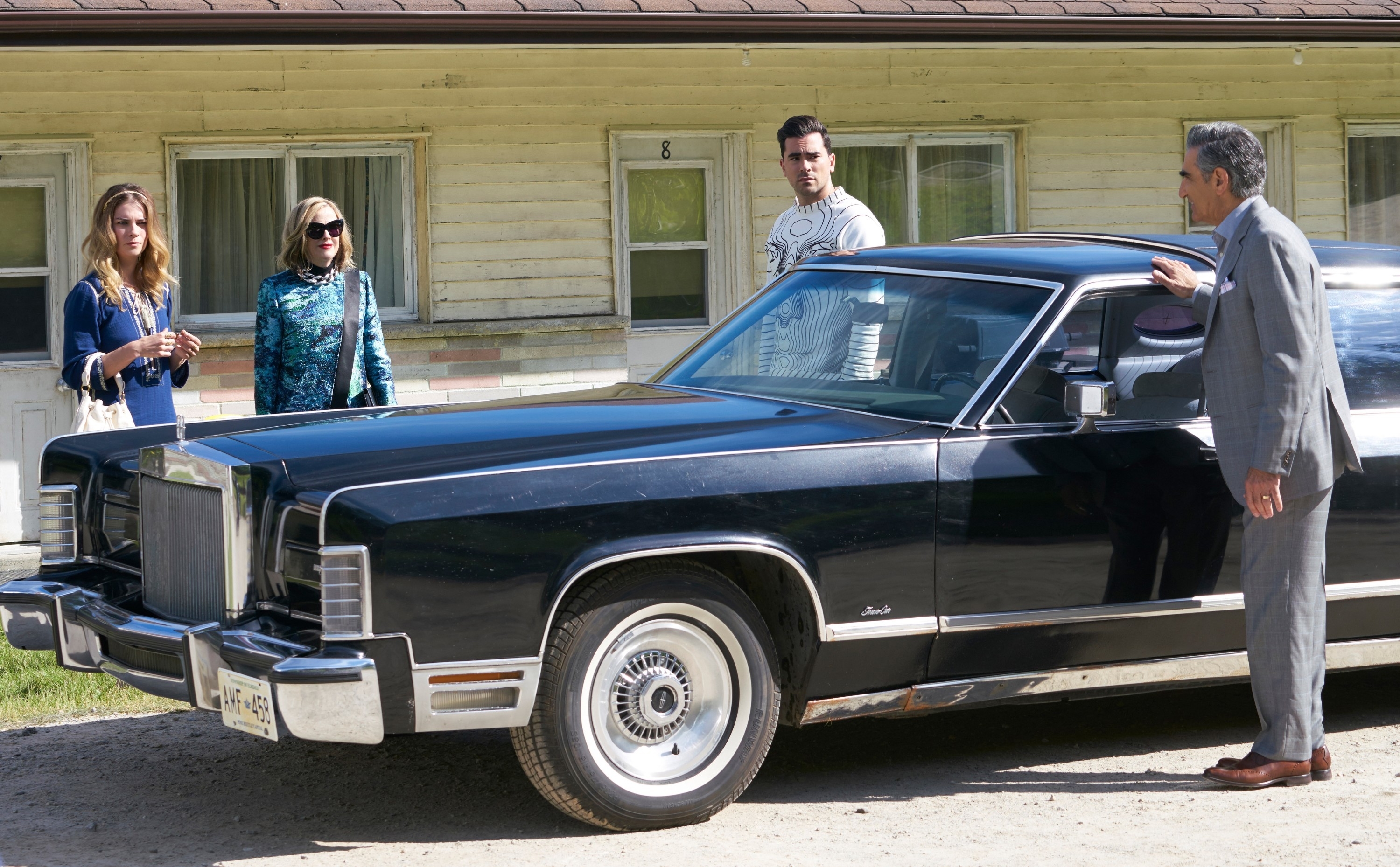 Annie Murphy, Catherine O'Hara, Daniel Levy, and Eugene Levy stand by a classic black car in front of a motel