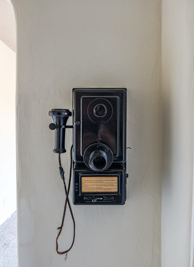 Vintage wall-mounted telephone with a rotary dial, earpiece, and a small plaque for instructions. No people are present in the image