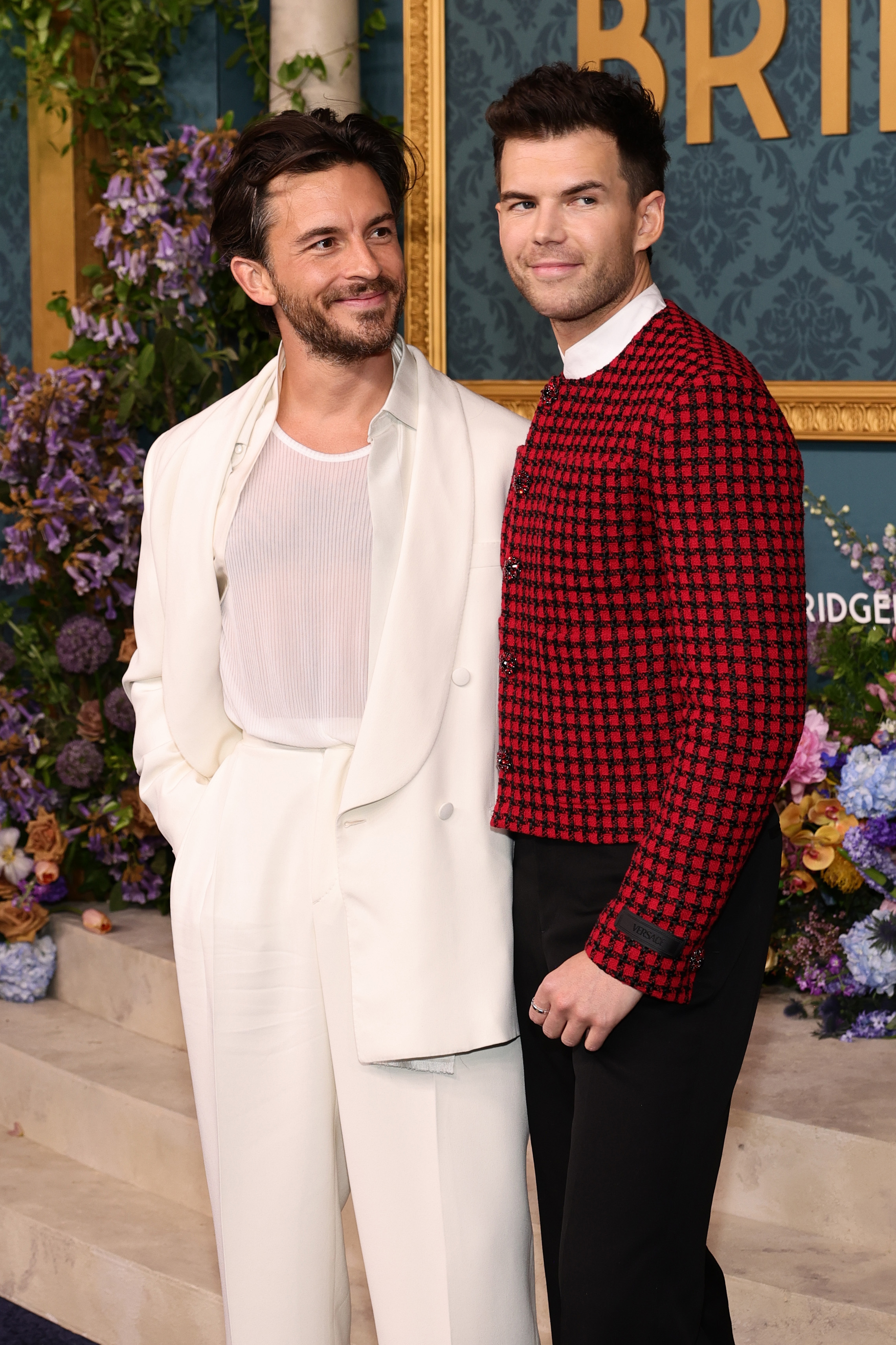Jonathan Bailey and Luke Newton at a formal event, with Jonathan in a suit and Luke in a red and black checkered jacket and black pants