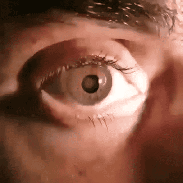 A close-up of a human eye fully opening, revealing a brown iris