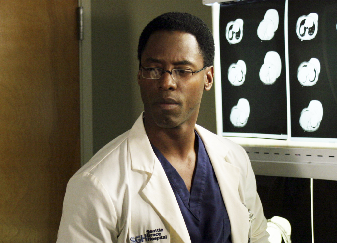 Isaiah Washington in a lab coat stands by a series of brain scans on a TV set