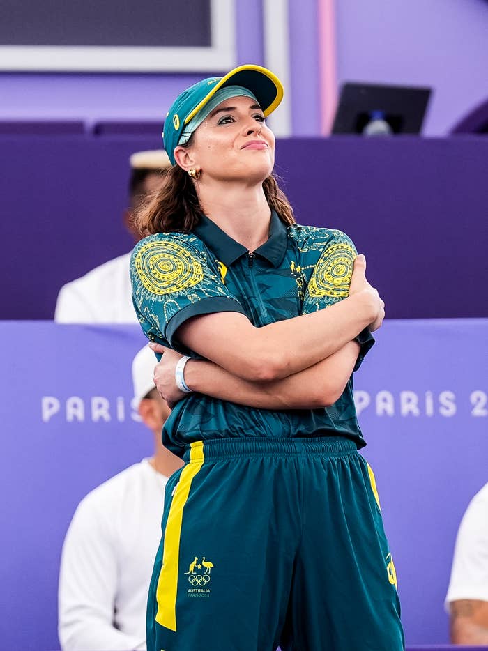 Rachael Gunn is seen standing with arms crossed, wearing an Australian team uniform and cap, at a sporting event in Paris, with "Paris 2024" visible in the background