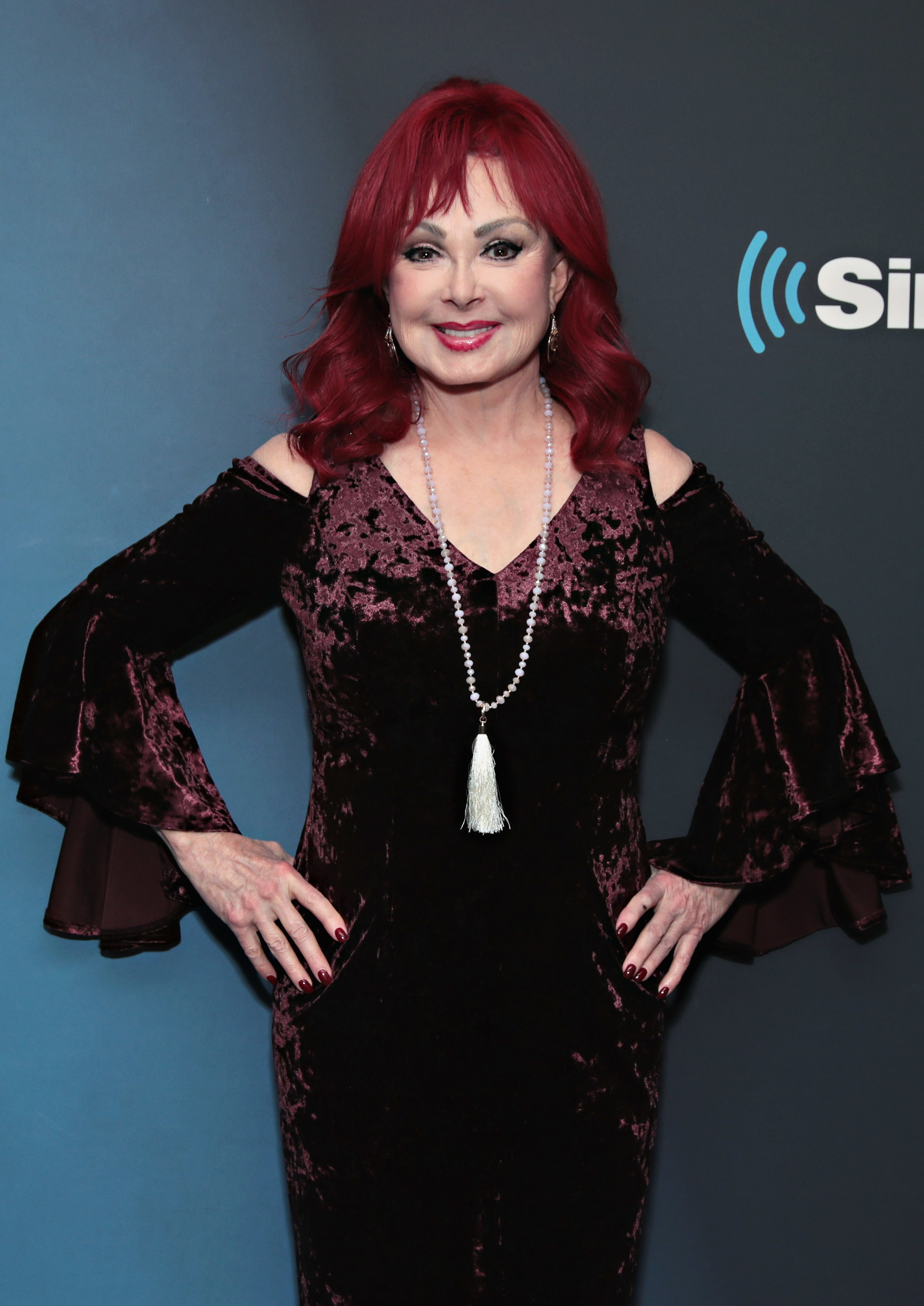 Naomi Judd on the red carpet wearing an elegant, off-the-shoulder velvet dress with bell sleeves and a long pearl necklace