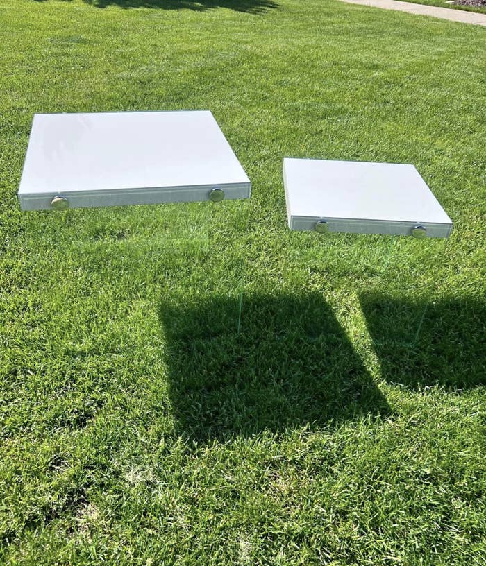 Two rectangular white objects levitate above a grassy lawn, casting shadows on the grass below