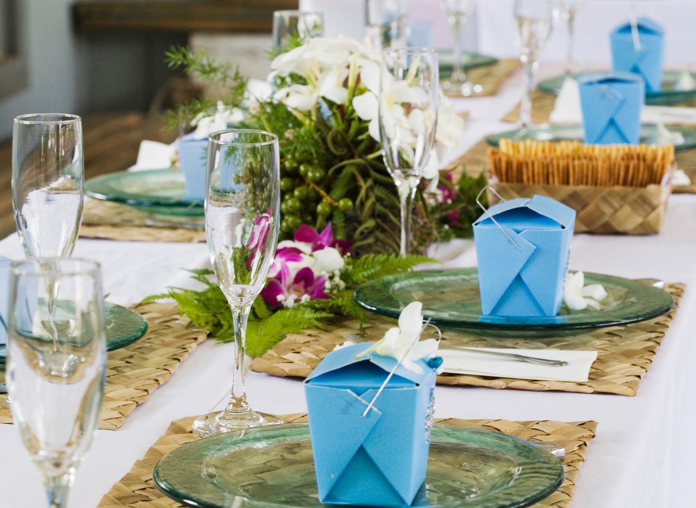 Elegant table setting with glasses, plates, blue gift boxes, and floral centerpiece on dining table
