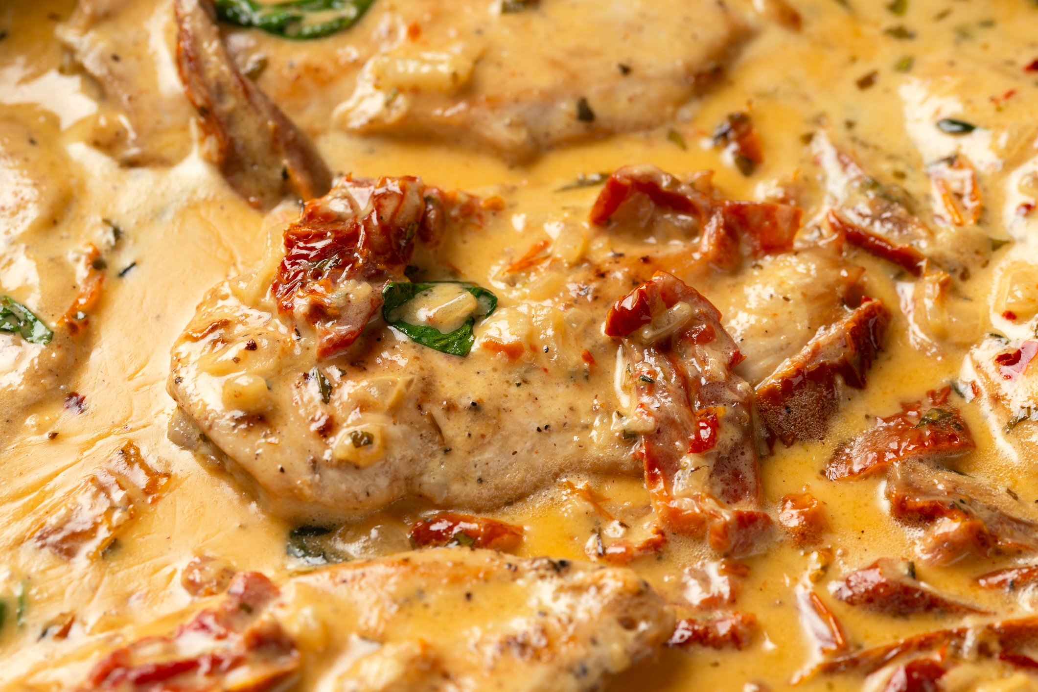 Close-up of a creamy garlic chicken dish with sun-dried tomatoes and herbs. The chicken pieces are surrounded by a rich, thick sauce