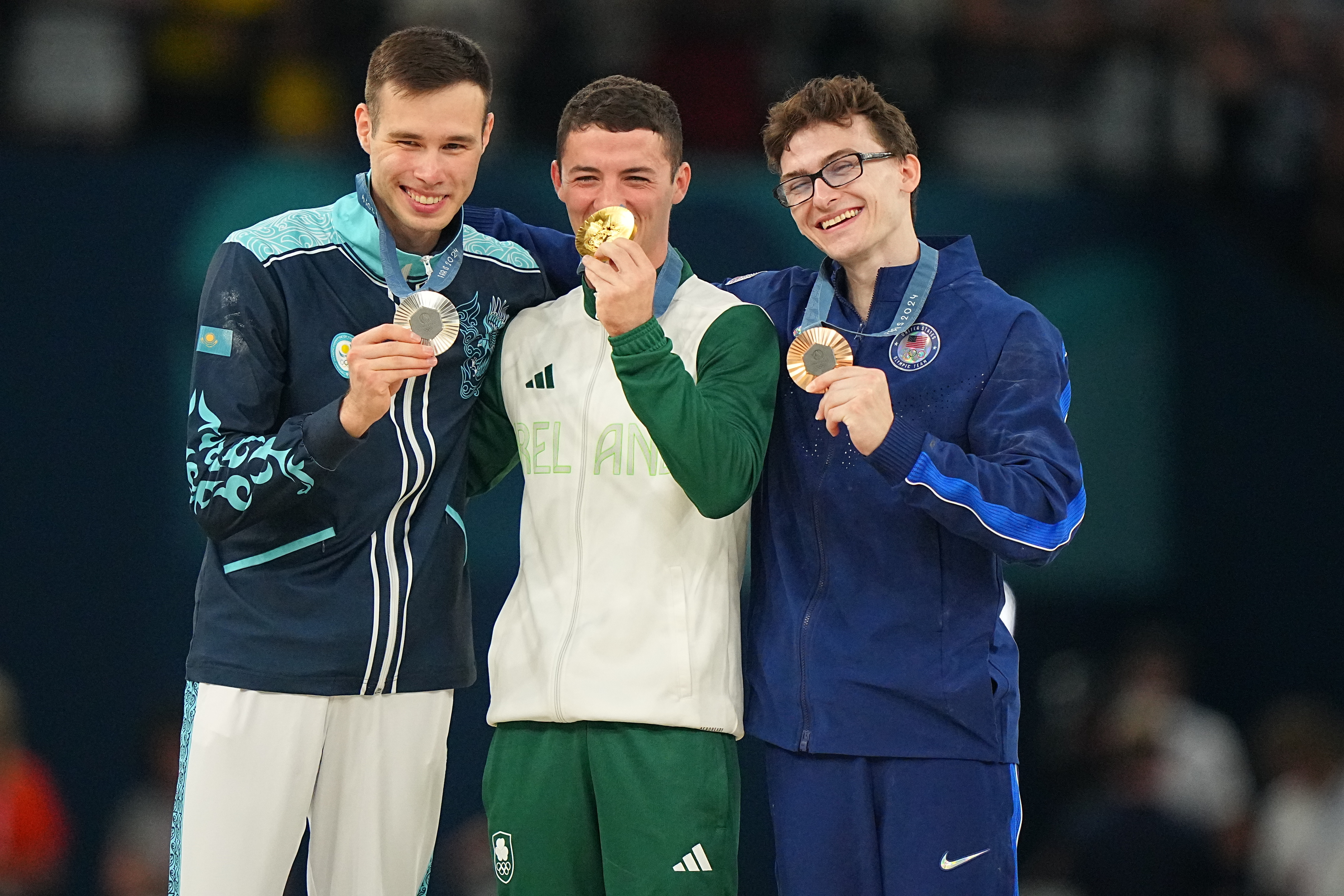 Smiling athletes Yulo, Bobrov, and Ivanov pose with their medals: silver, gold, and bronze, respectively, at an indoor sports event