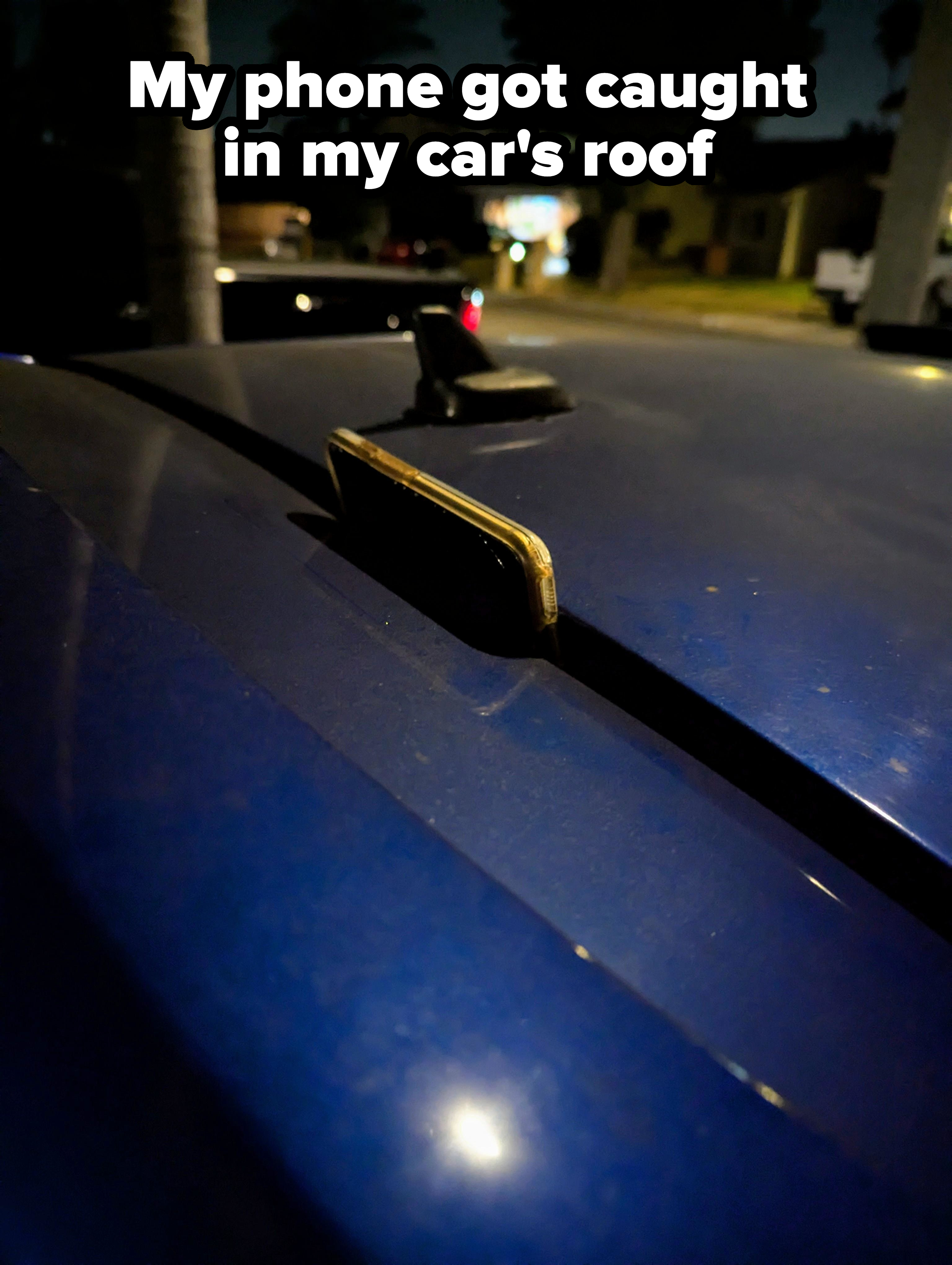 A close-up of a mobile phone, with a weathered case, placed on the roof of a car at night in a residential neighborhood