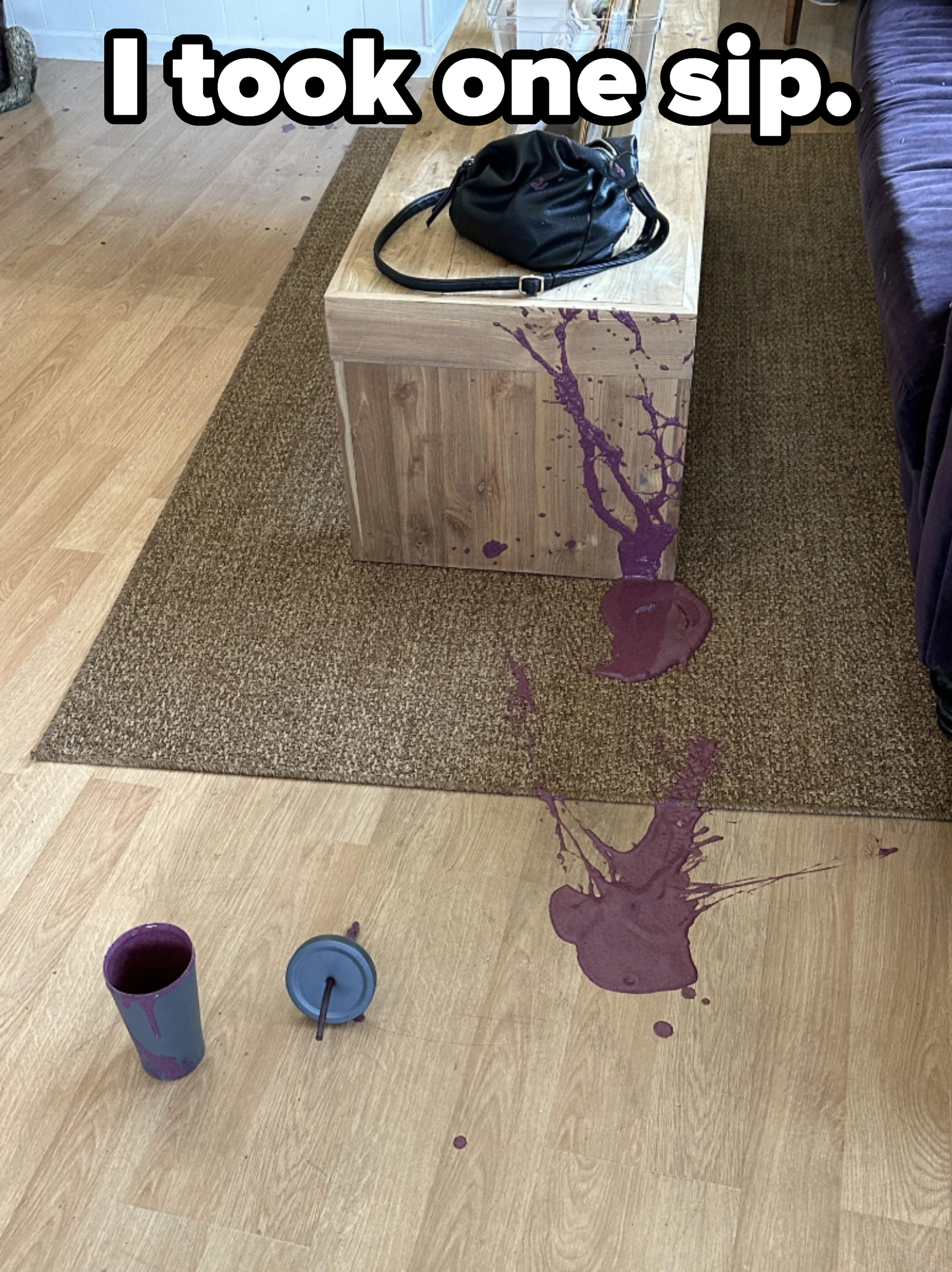 Spilled drink on a wooden table and carpet. Items visible include a black bag, two glass cups on the table, and spilled liquid with a knocked-over cup and lid on the floor