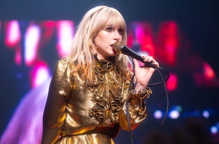 Hayley Williams performing on stage, wearing a shiny, ruffled outfit while holding a microphone