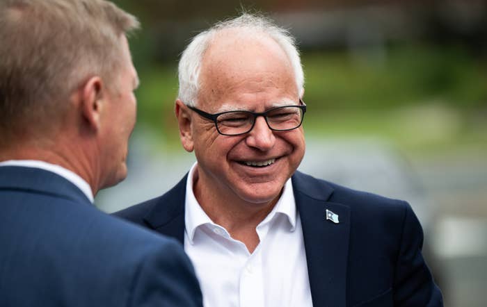 Two men in conversation, one is turned to the side and the other, wearing glasses, is smiling