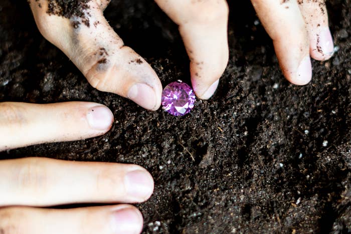 Hands digging in soil, revealing a bright purple gemstone