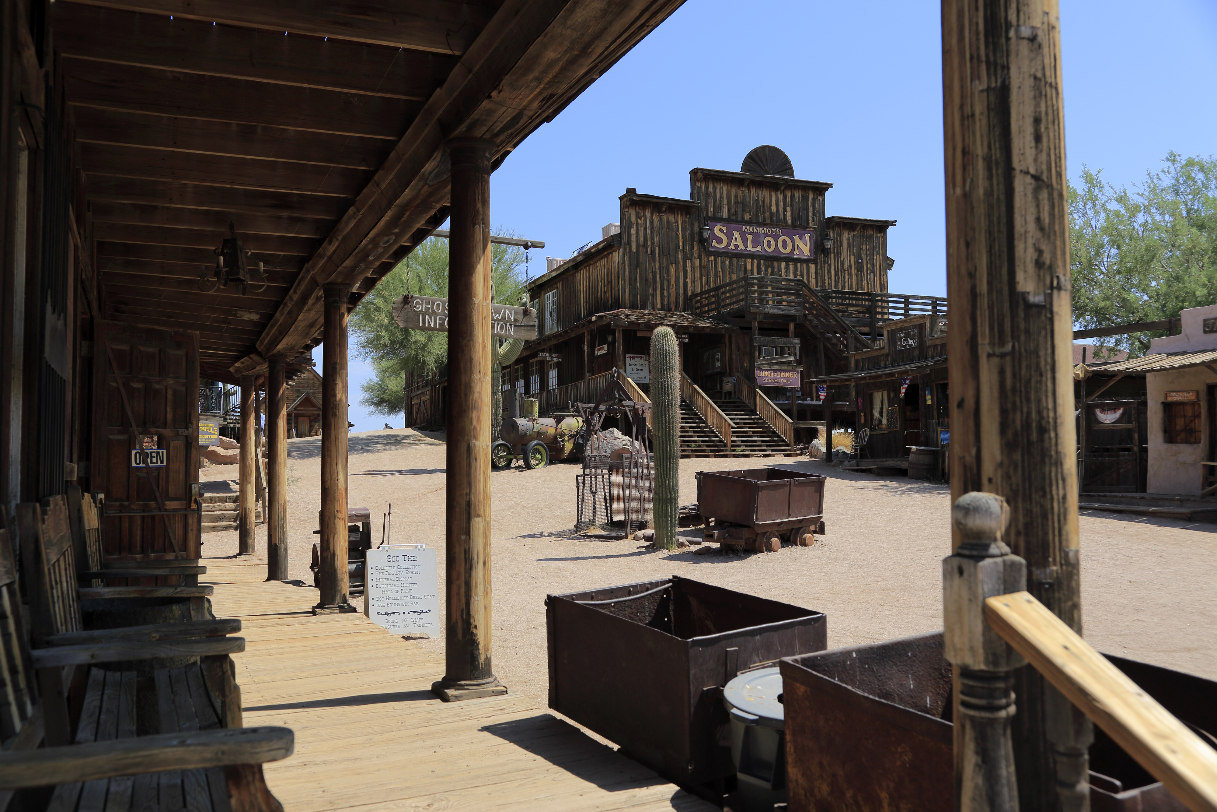 An empty wooden sidewalk leads to an old Western-style saloon and other rustic buildings in a deserted town with a visible wooden sign for an inn